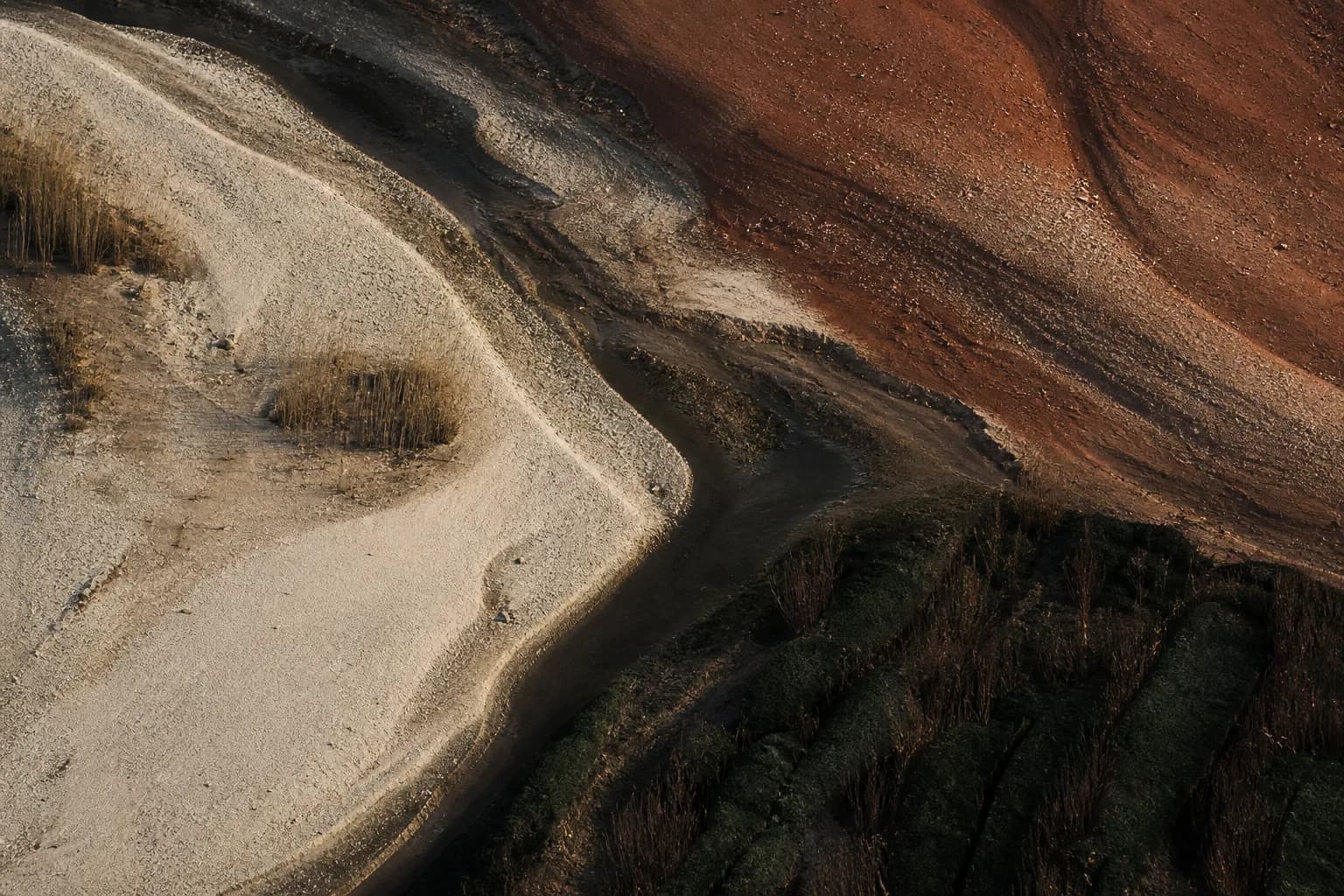 Vista aérea de água escura atravessando camadas de solo calcário, terracota e vegetação profunda.